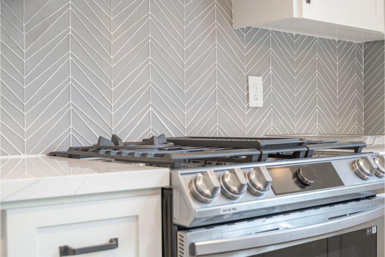 Custom gray shaker cabinets in contemporary San Jose kitchen with elegant herringbone tile backsplash and stainless steel appliances